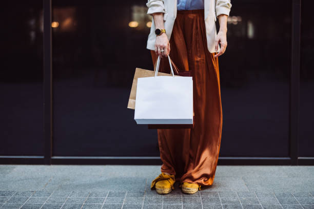 An Anonymous Woman Carrying Shopping Bags Outdoors Unrecognizable businesswoman holding paper bags while standing at the city street. brown leg stock pictures, royalty-free photos & images