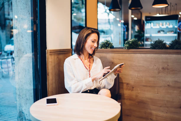 istock Focused elegant woman using tablet in cafe near glass wall 1407472095