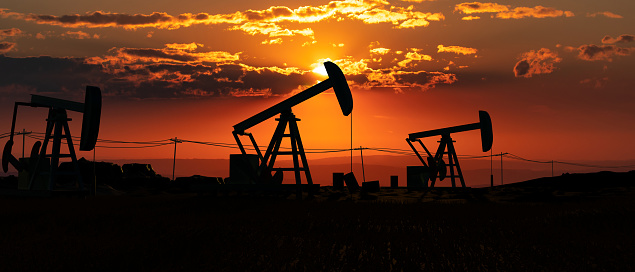 Silhouette of oil pumps. Landscape like Texas with glowing sky during sunset and some clouds. Oil and gas industry, drilling and oil production. concept. 3D illustration