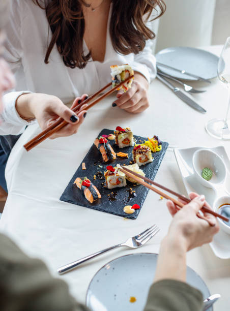 istock Women taking sushi from plate with chopsticks, eating in fine dining restaurant 1407475404