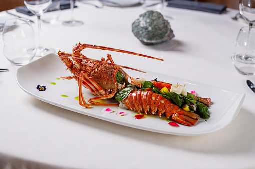 Lobster serving on a rectangular plate, cut in half and filled with spinach and vegetables, table in fine dining