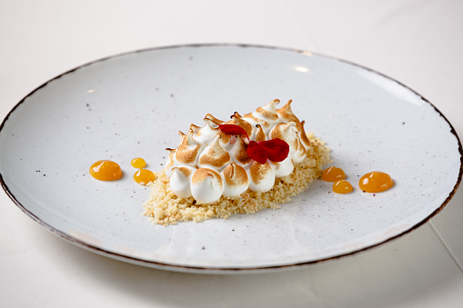 Dessert served on plate in fine dining, crumbs covered with spiky cream and decorated with caramel cream and red petals