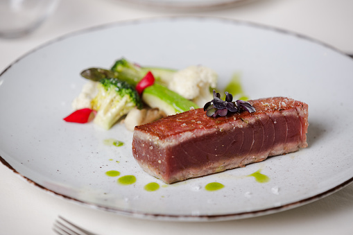 Tuna steak with vegetables on plate in fine dining restaurant, table place setting