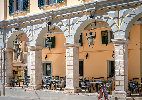 Corfu, Greece - June 3 2022: Arcaded neoclassical building with sidewalk cafes in N. Theotoki St, a famous pedestrian retail street in the old town that runs to the Liston and Spianada Square.