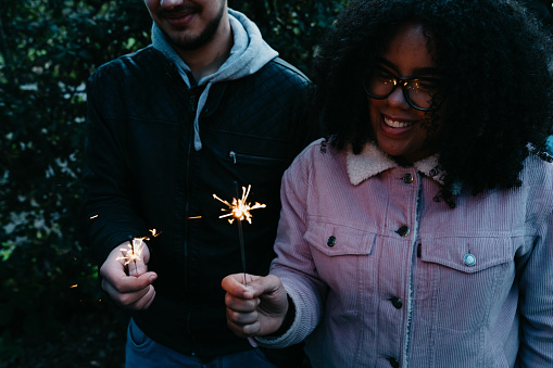 Two friends celebrating together with sparklers outdoor. Multi ethnic people.