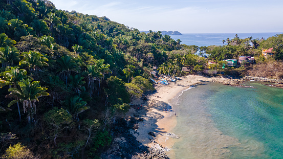 Drone point of view on hidden small beach, surrounded by tropical palm trees in San Pancho, Nayarit, Mexico.