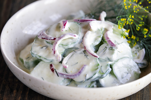Overhead view of easy creamy Greek yogurt cucumber salad made with cucumbers, lemon zest, red onions and fresh dill. Extreme selective focus with blurred foreground and background.