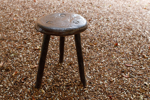An old wooden stool on a gravel surface.