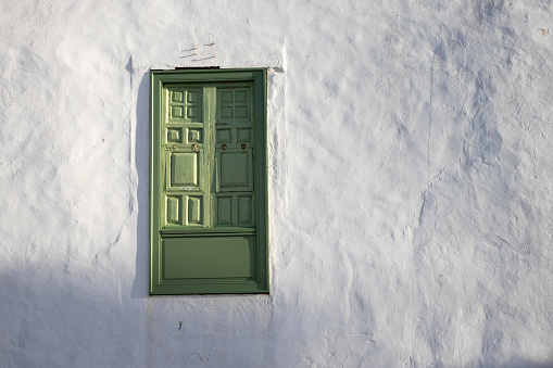 Old traditional wooden shutter on a window, always painted green at the island. White color of the facade. Street of the old city Teguise, Lanzarote, Canary Islands, Spain.