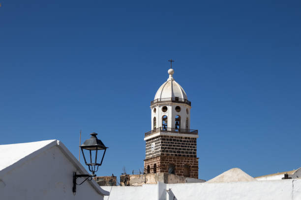 Old black lantern and a tower of a church named Church Iglesia de Nuestra Senora de Guadalupe. Bright blue sky. Teguise, Lanzarote, Spain.