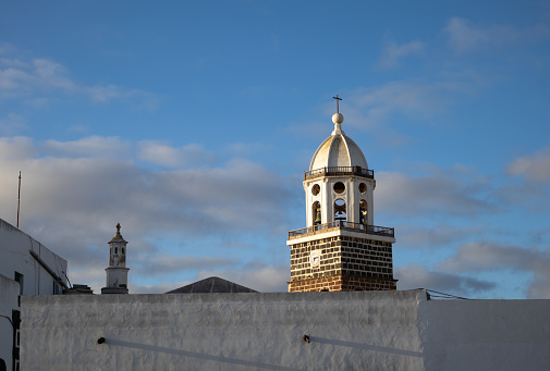 Early spring evening. Clouds enlighted by the sunset on a blue sky. Tower of a church named Church Iglesia de Nuestra Senora de Guadalupe. Teguise, Lanzarote, Spain.