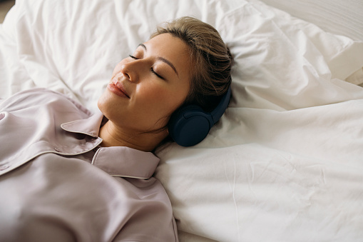 A from above view of a happy Asian female in pajamas napping peacefully with  headphones on her head.