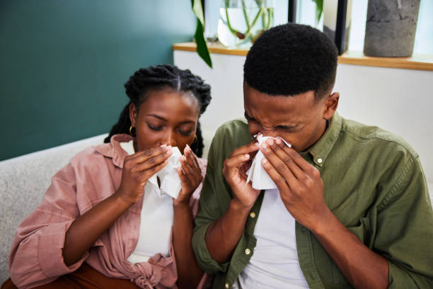 istock Young couple with colds sneezing into tissues while sitting at home 1407499110