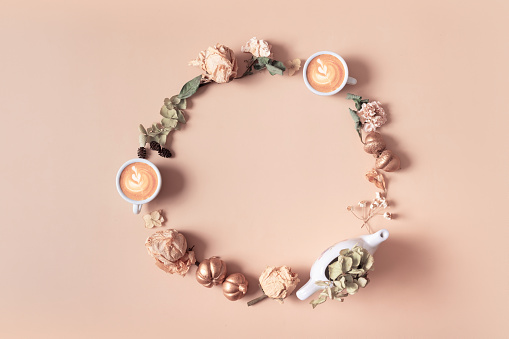 Autumn composition. Wreath made of dried leaves and coffee cups on pastel beige background. Autumn, fall concept. Flat lay, top view, copy space.