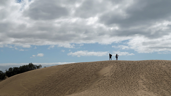 Hot dry sand dune and beach at Maspalomas with two adult people in silhouette walking up it in the distance. Summers day outdoors, Gran Canaria, Canary Islands, Spain, July 1, 2022