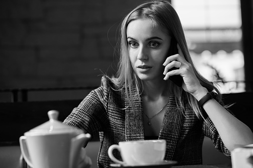 angry serious young woman in cafe with mobile phone talking, monochrome