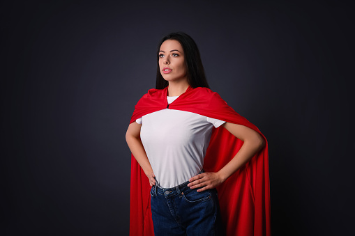 Confident young woman wearing superhero cape on grey background