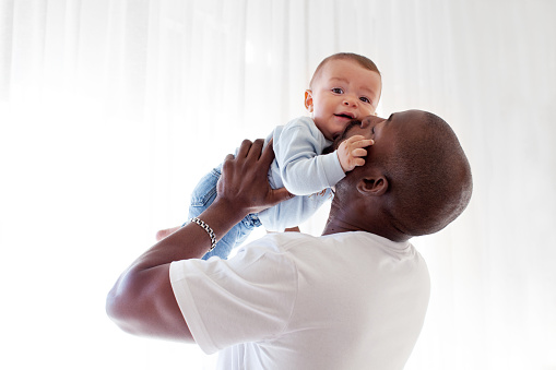 African American black dad kisses, holds on arms and loves baby son mixed race child against white background