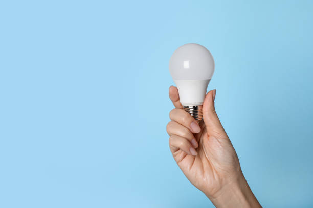 istock Woman holding LED light bulb on blue background, closeup. Space for text 1407507386