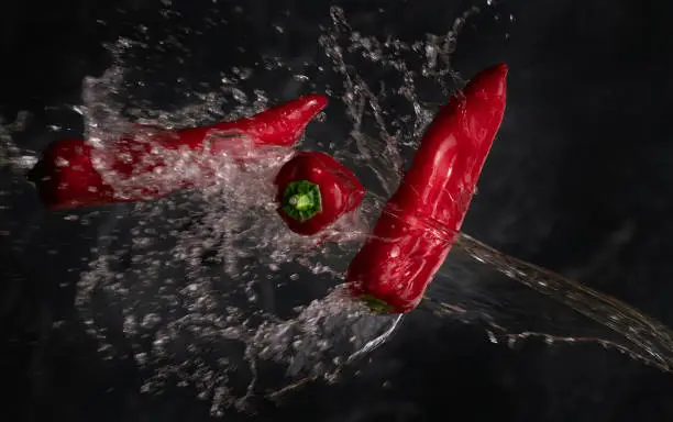 Photo of Close-up of red peppers being splashed with water against a dark background.