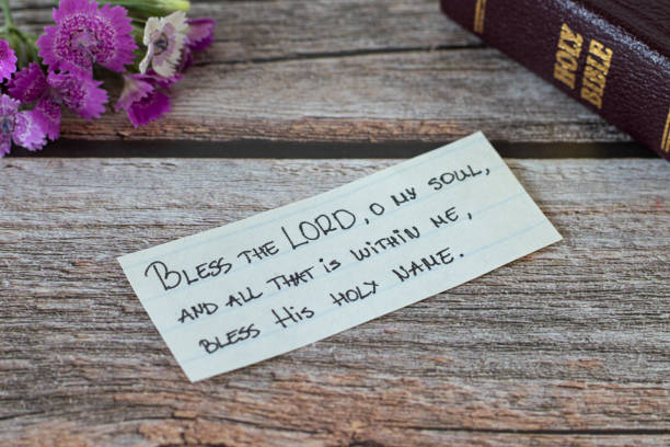 Handwritten note with Christian text verse and a closed Holy Bible book on a wooden table with flower stock photo