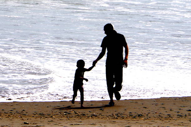 Aichi, Japan – May 17, 2015: It is a family to play with the waves on the beach.Here is the Long Beach of Aichi Prefecture, Tahara.Japan.\nDaughter and son pull the hand of a young father, playing with the waves.