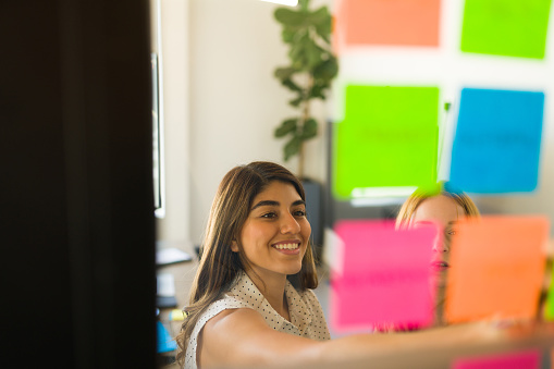 Cheerful young woman writing on colorful neon sticky notes and working on brainstorming with co-workers