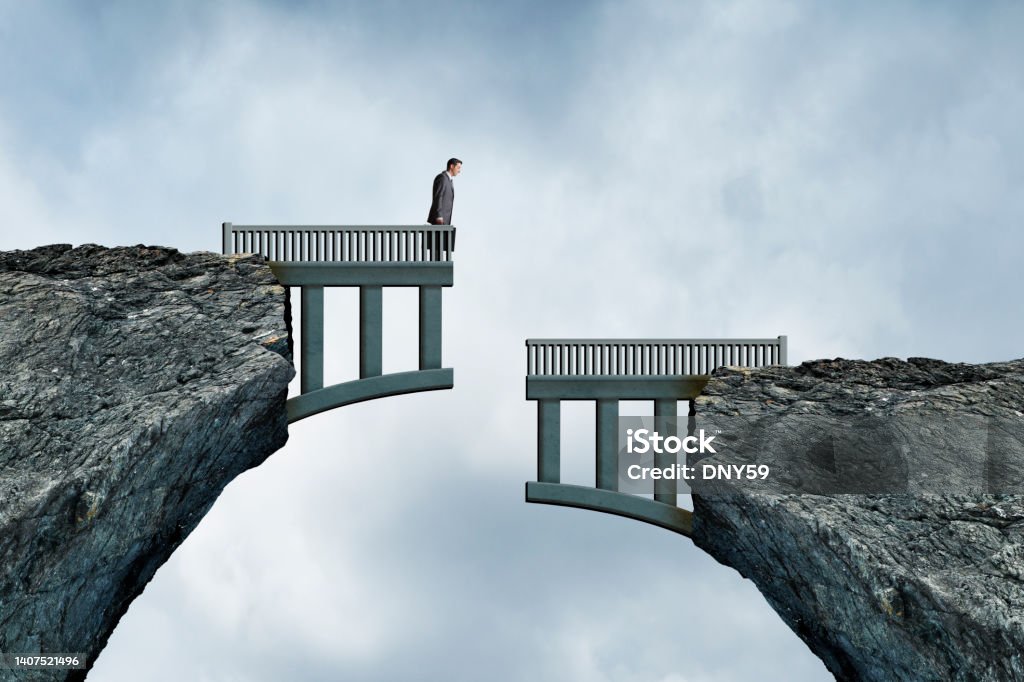 Mismatched Bridge Construction A man holding a briefcase looks down at the other half of the bridge that doesn't align with the side he is standing on. Separation Stock Photo