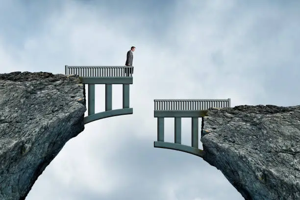 A man holding a briefcase looks down at the other half of the bridge that doesn't align with the side he is standing on.