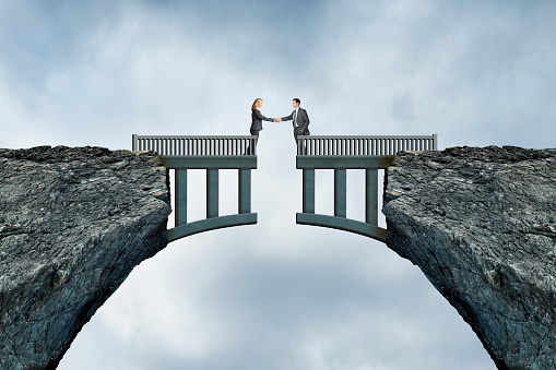 A man and a woman shake hands as they stand on opposite sides of a bridge separated by a missing gap.