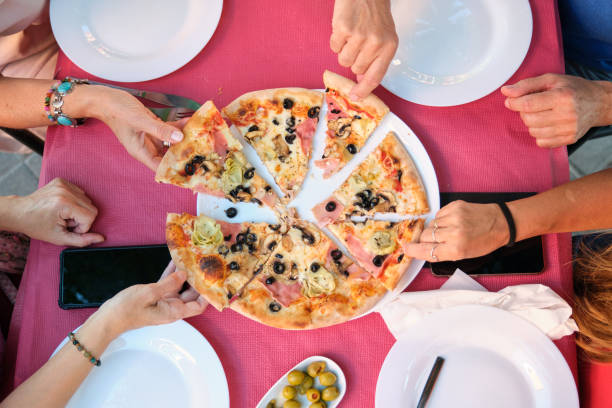Top view of mature friends hands taking a slice of pizza at a restaurant table.