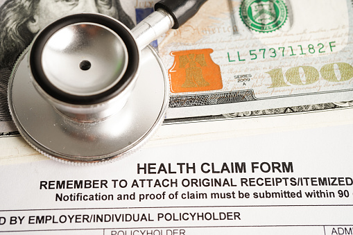 Health claim form with stethoscope and US dollar banknotes, insurance accident medical concept.