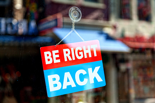 Red and blue sign in the window of a shop saying Be right back.
