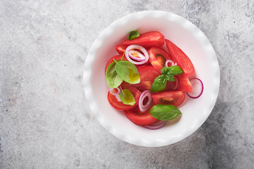 Fresh tomatoes salad with basil leaves, olive oil and onion in white bowl on light background. Traditional italian or mediterranean food diet. Top view.