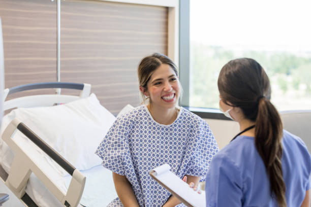 junge erwachsene patientin erhält gute nachrichten von krankenschwester - hospital patient bed doctor stock-fotos und bilder