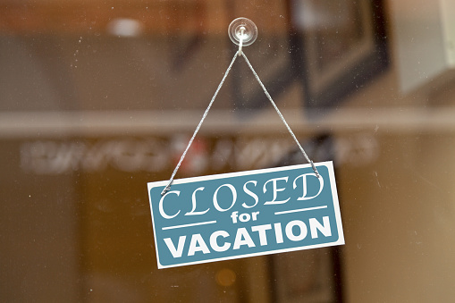 Blueish sign hanging at the glass door of a shop with written in it Closed for vacation.