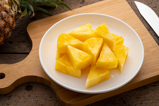 Fresh delicious pineapple cut into pieces on white plate on a wooden table