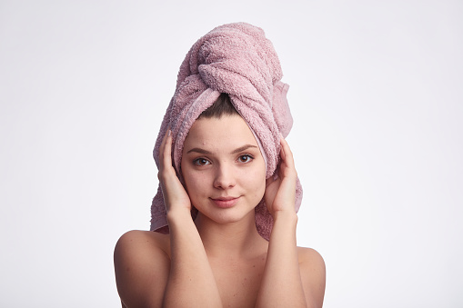 Young attractive woman with towel on her head looks at the camera and smiles on white background with copy space for text. Face care and hair concept