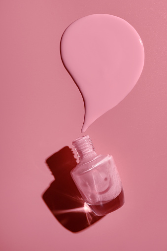 overturned bottle with pink nail polish on a pink background.