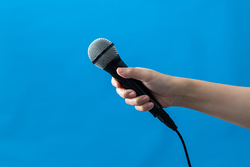 Hand holding a microphone on blue background.