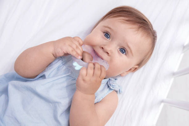 istock Infant baby girl bites silicone teether in her bed. View from the top 1407557684
