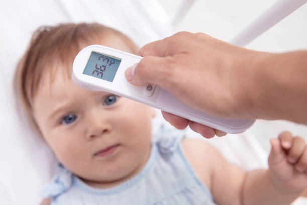 mother checks baby's  temperature with modern electronic termomether at baby's forehead - infrared thermometer imagens e fotografias de stock