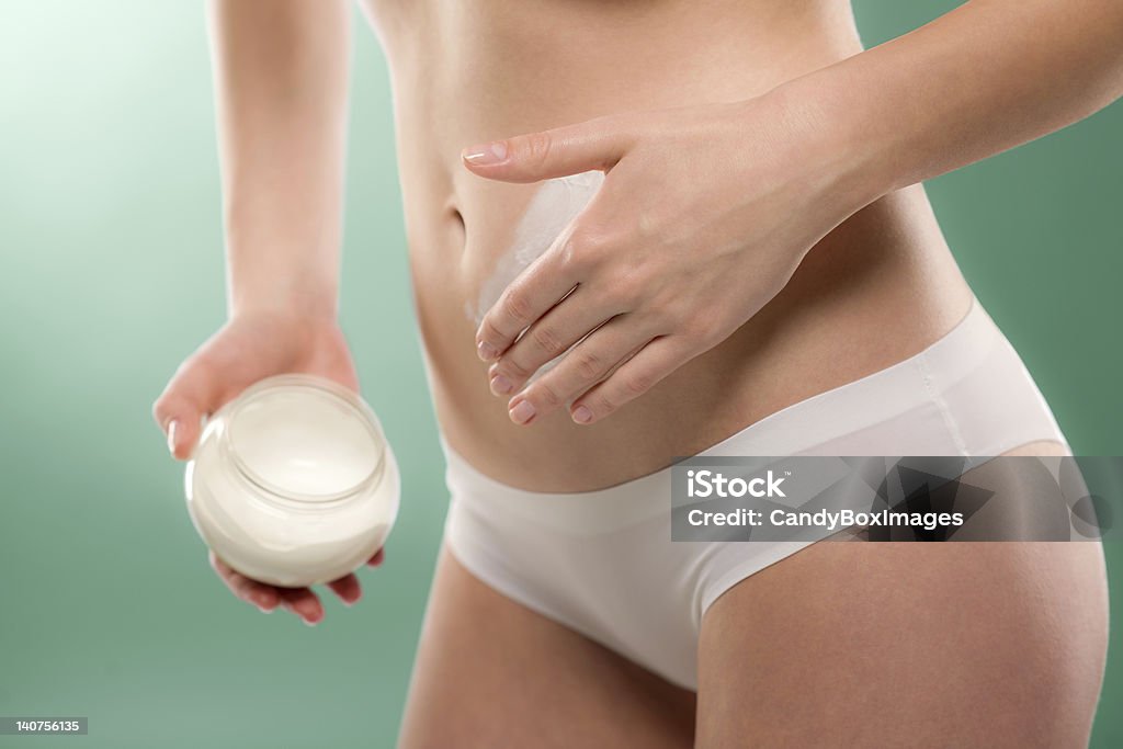 Woman apply body cream on belly Woman apply body cream on belly slim silhouette on green Moisturizer Stock Photo