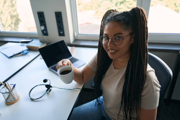 Cheerful company employee drinking caffeinated beverage seated at desk