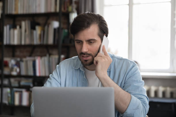 istock Serious businessman looks at laptop while talks on smartphone 1407561774