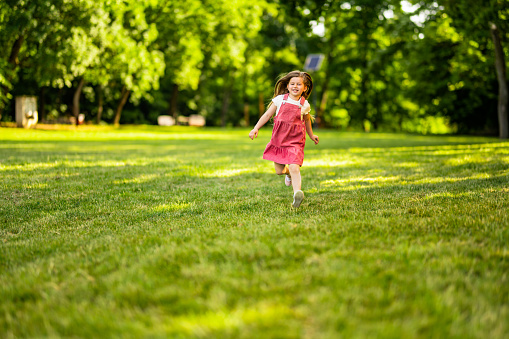 Playful girl running and having fun at the public park on a spring day.