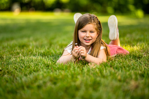 Close up portrait of beautiful little girl with blonde long hair and big blue eyes looking at camera with relaxed expression. Nature background.