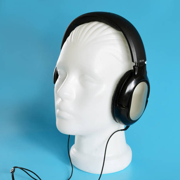 Plastic white mannequin head with musical stereo headphones, close-up on a blue background