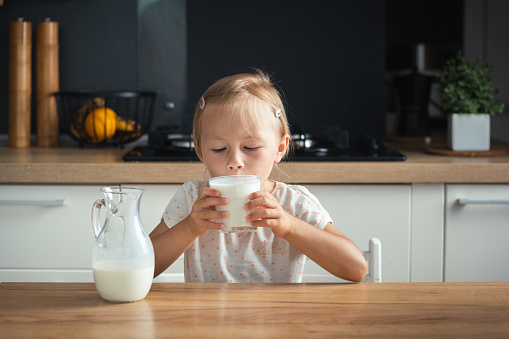 Happy African-American girl with glass of milk looking at camera on background of her father and sister