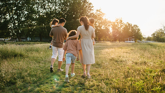Rear view of family with three children walking on the grass field during sunset.
